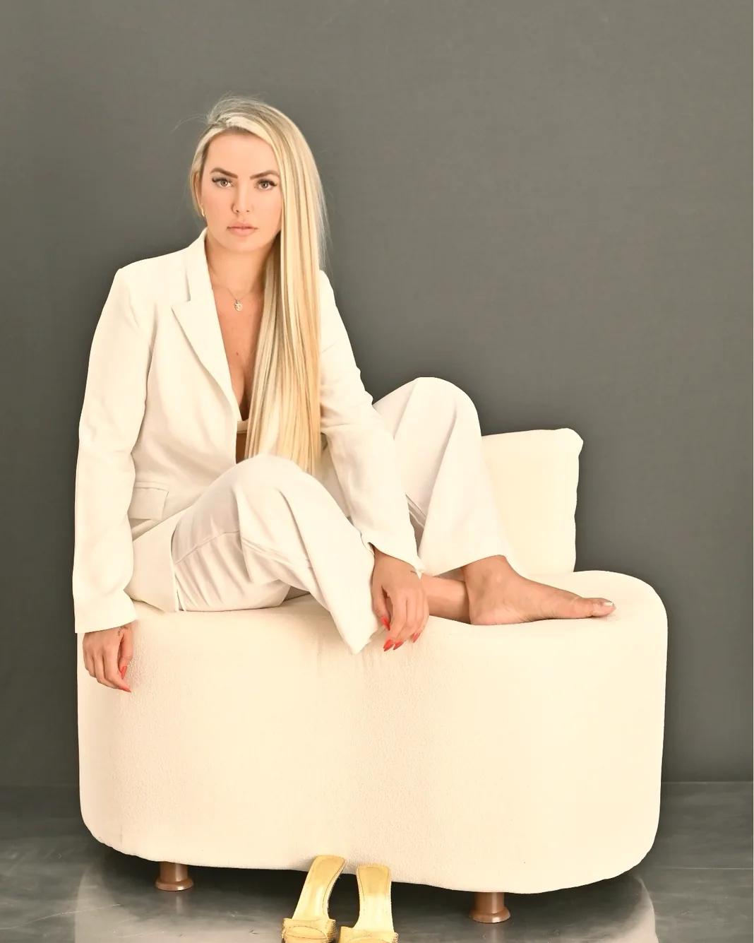 Graziele Dalpra, de terno branco, sentada em uma poltrona clara