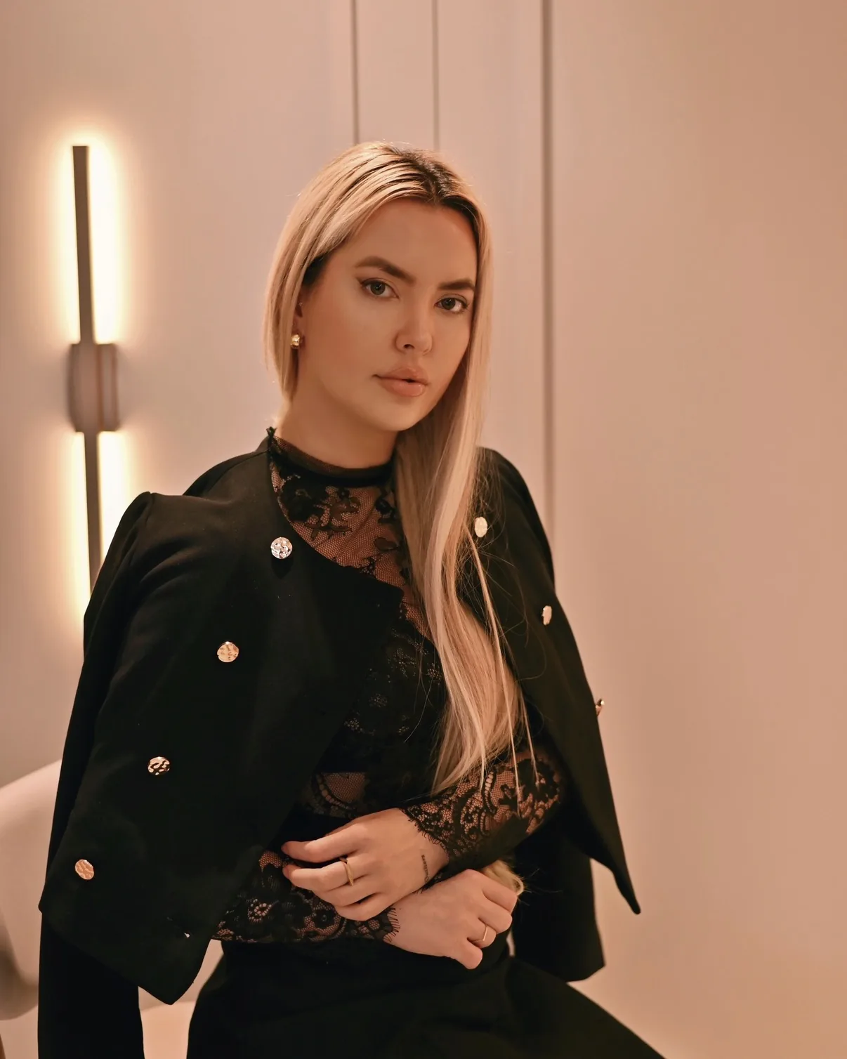 Graziele Dalpra de preto, com blusa de renda e jaqueta nos ombros, olhando para a câmera