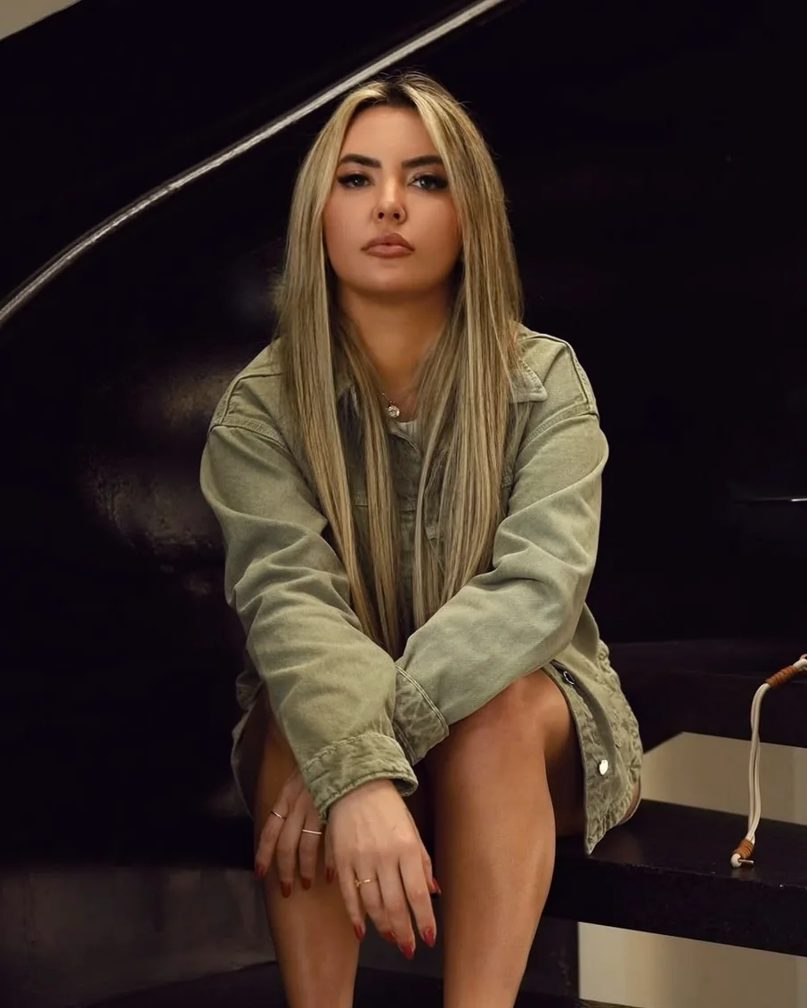 Graziele Dalpra sentada numa escada escura, de jaqueta verde