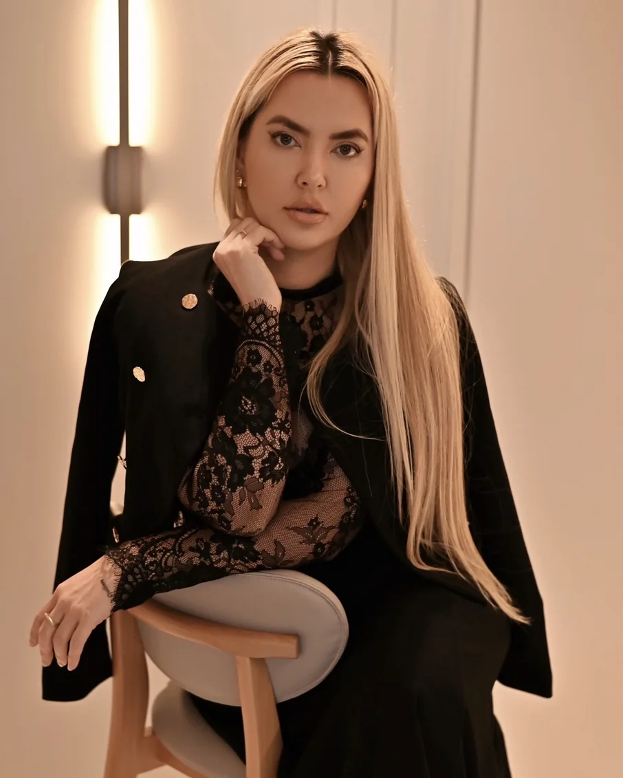 Graziele Dalpra de preto, com blusa de renda, sentada e com a mão no queixo